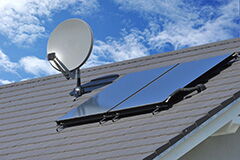 Satellitenschüssel und Solarkollektor auf grauem Dach unter blauem Himmel mit Wolken